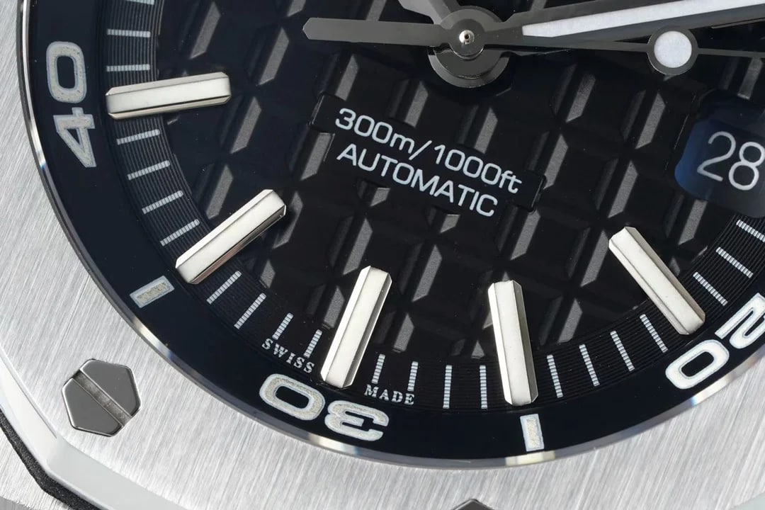 Close-up of the dial: the raised squared pattern, applied baton markers, the printed block with its two lines, the date at three, the dive numerals on the inner ring and the line at six