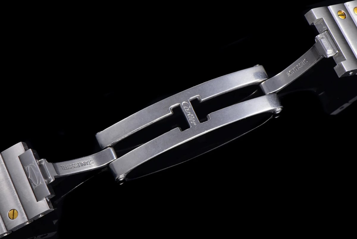 Clasp detail with the folding clasp opened flat against the dark background, engraved lettering running along its blades, and the bracelet links with their gold-toned screw heads laid out beside it