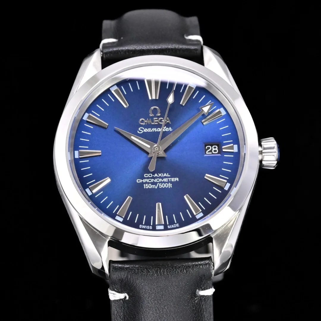 Blue dial straight on with applied wedge markers carrying pale luminous fill, the brand and line names above the centre, a date aperture at three and a black textured leather strap