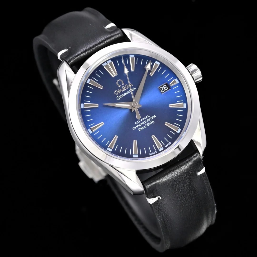 Angled three-quarter view of the case turned so the sloping bezel and the crown at the right catch the light, the blue dial's markers lit along their tops and the black textured strap curving away below in a gloved hand.