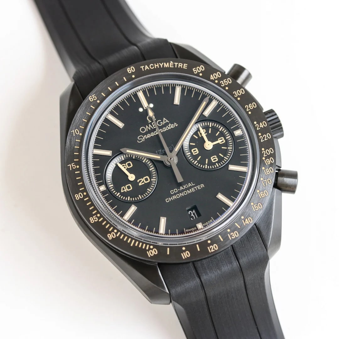 Angled view of the black case and strap, with the crown and two pushers on the flank, the dial turned toward the camera and the tachymeter numerals running down the bezel