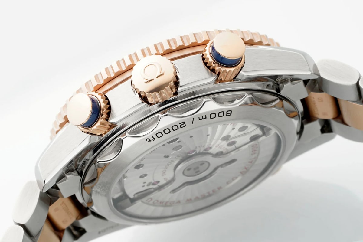 Case back detail with the transparent window showing a round gold-toned element across the centre, engraved lettering around the rim, the scalloped edge and the bracelet folded out to the right
