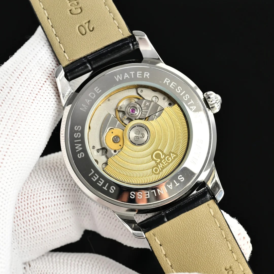 Case back detail with the watch turned over in a gloved hand: the transparent back framed by a ring of engraved lettering, parts visible through it in striped and polished finishes, and the black strap folded behind with its pale tan lining facing the camera