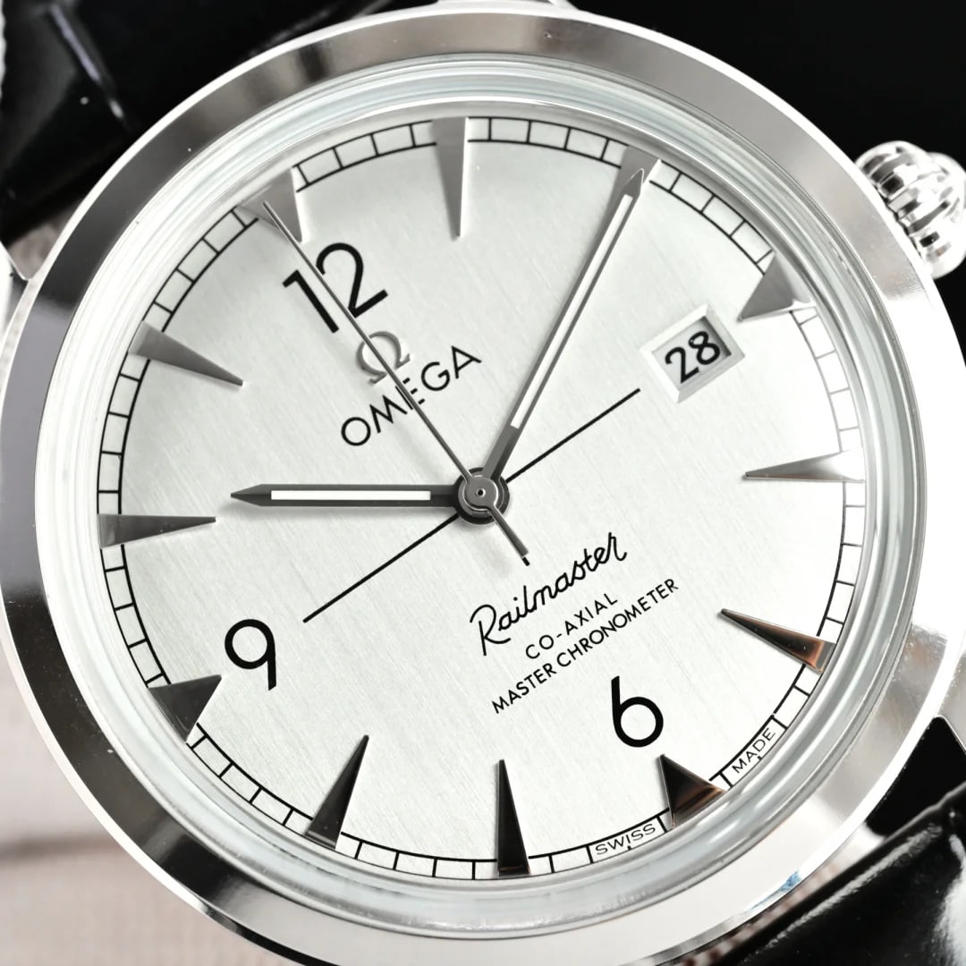 Dial close-up: the numeral twelve, the brand name with its logo, the script line name, the two-line Master Chronometer wording, arrow-shaped markers with a pale recessed fill, and the date window showing two digits at the right