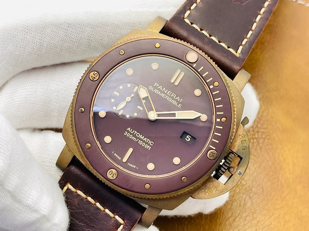 Three-quarter angled view of the case and brown dial, showing the bronze-toned case flank and the crown-protecting bridge at the right, the date aperture at three o'clock and the dark brown stitched strap leaving the lugs