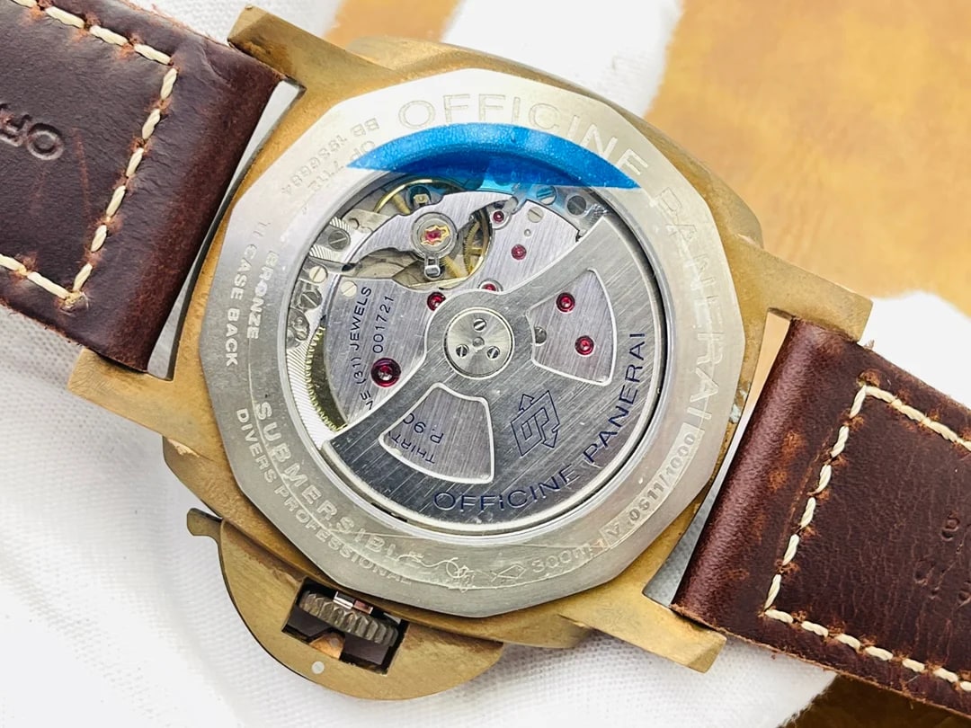 Case back detail with a transparent back showing what sits beneath it, a blue protective film laid across part of the surface, engraved lettering running around the rim and the dark brown strap folded behind the case