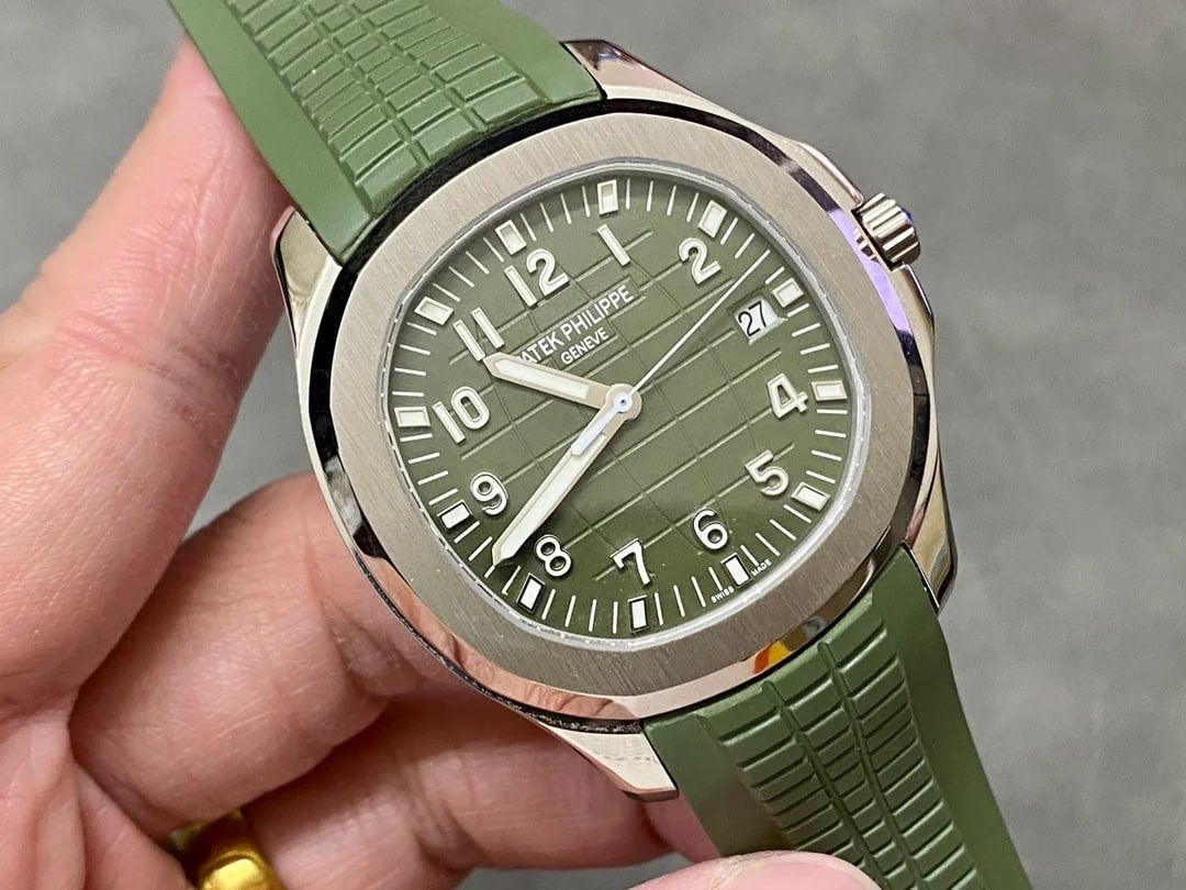 Three-quarter angled view with the case turned in the hand: the satin bezel flat and the polished flank both catch the light, the dial grid shifts across the green surface, the crown sits at the right and the green strap curves away below