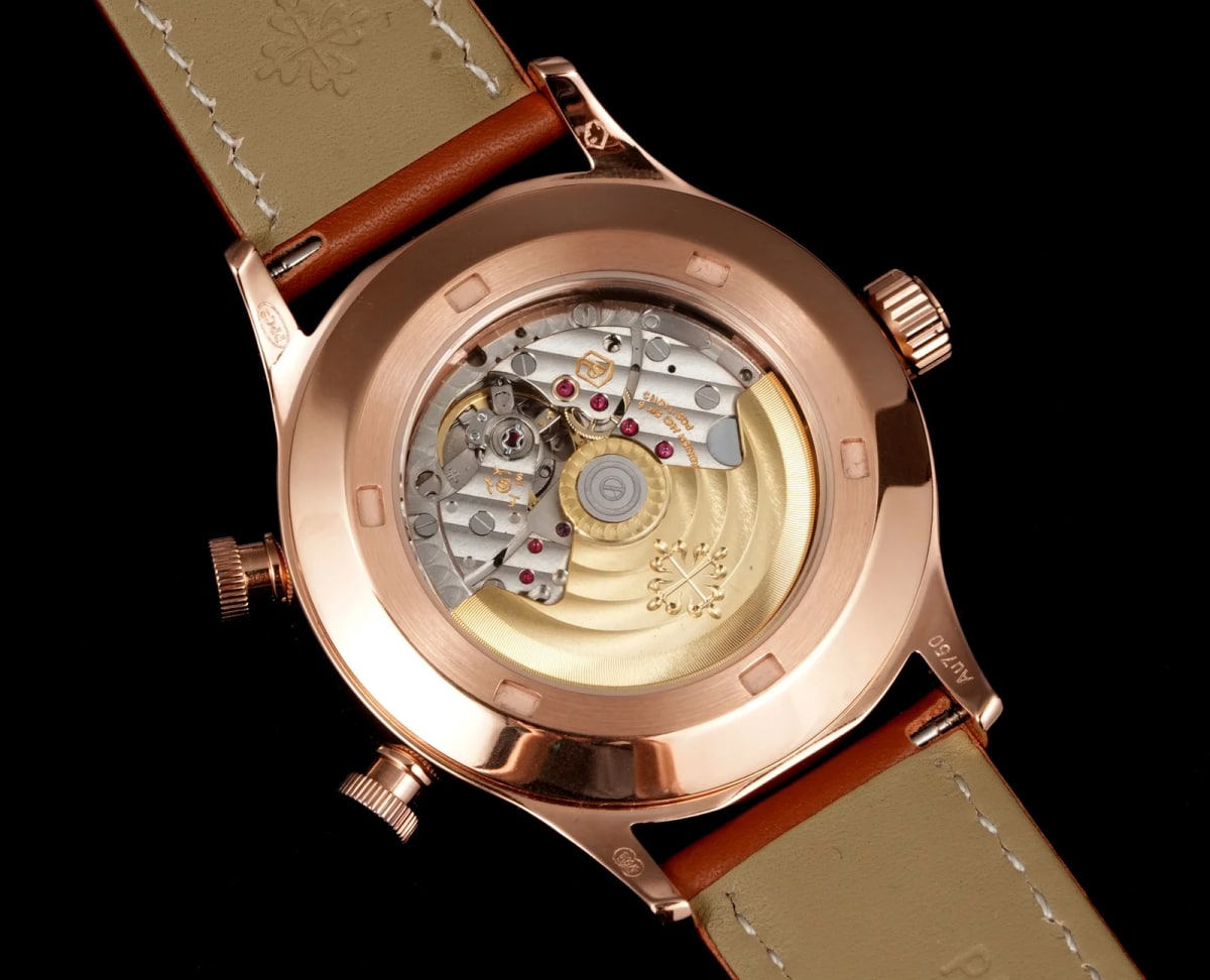 Case back detail with the round back of the gold-tone case catching the light and the brown leather strap turned away below it