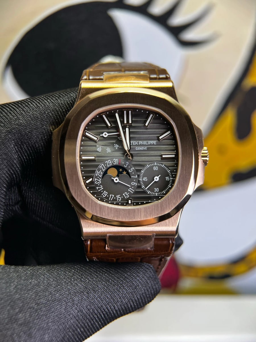 Ribbed brown dial straight on inside the gold-toned porthole case of a Nautilus, with a reserve sector high on the left and a small-seconds register beside a moon-phase aperture below, on a brown strap