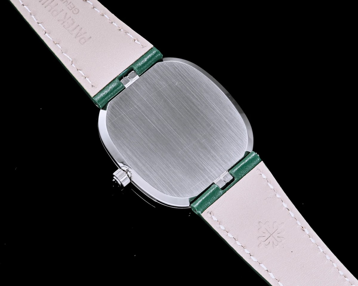 Case back detail filling the frame with a brushed elliptical back, the polished edge of the case running around it, the crown at the lower left and a green strap crossing behind