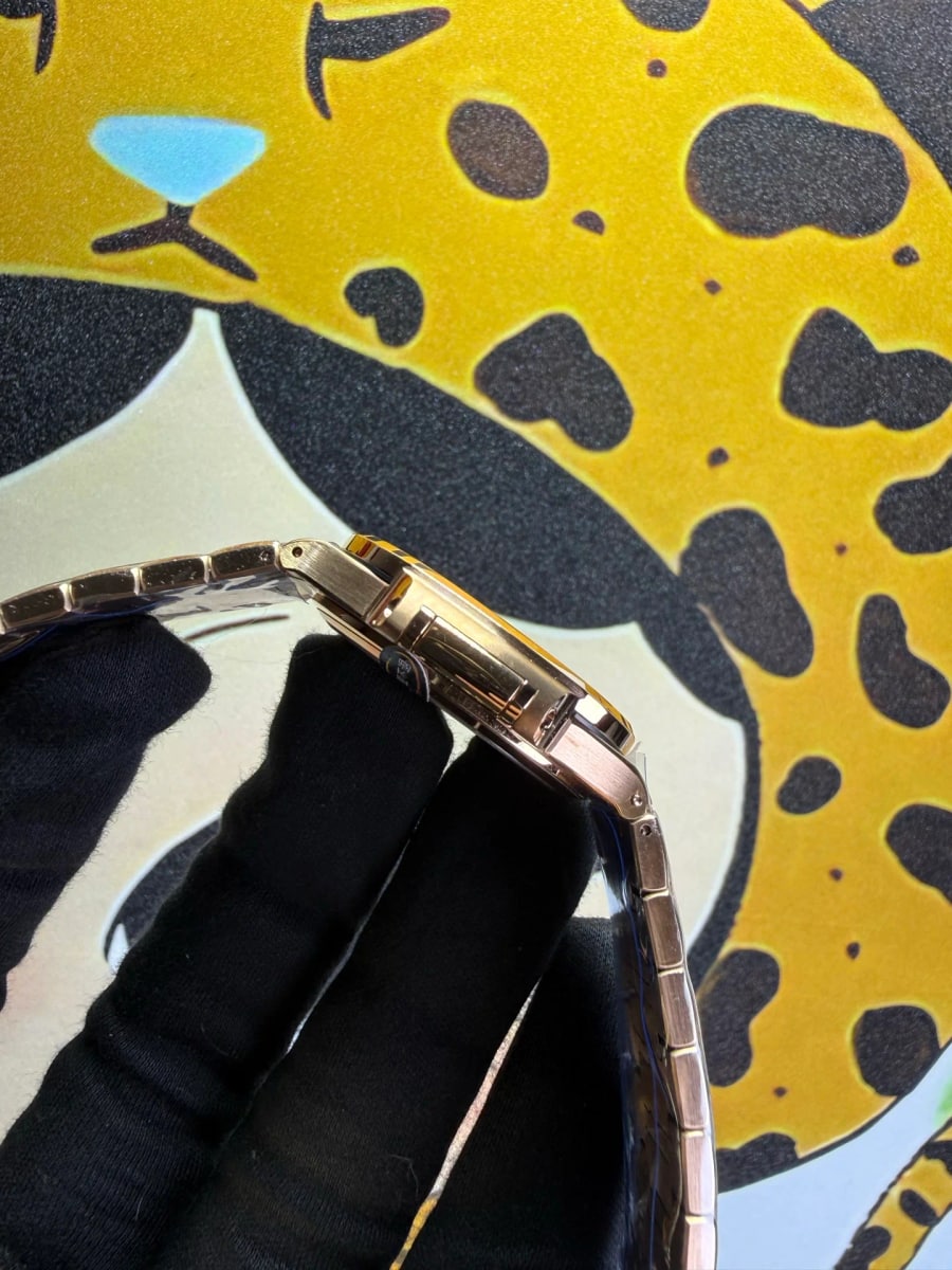 Clasp detail: the gold-tone bracelet links folded over a gloved hand with the clasp closed, showing the width of the bracelet against the small case