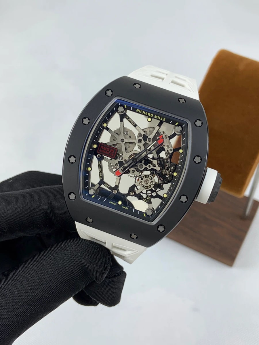 Angled three-quarter view of the matte black case, showing the bezel standing proud of the case top, the crown on the right side and the white strap turning down