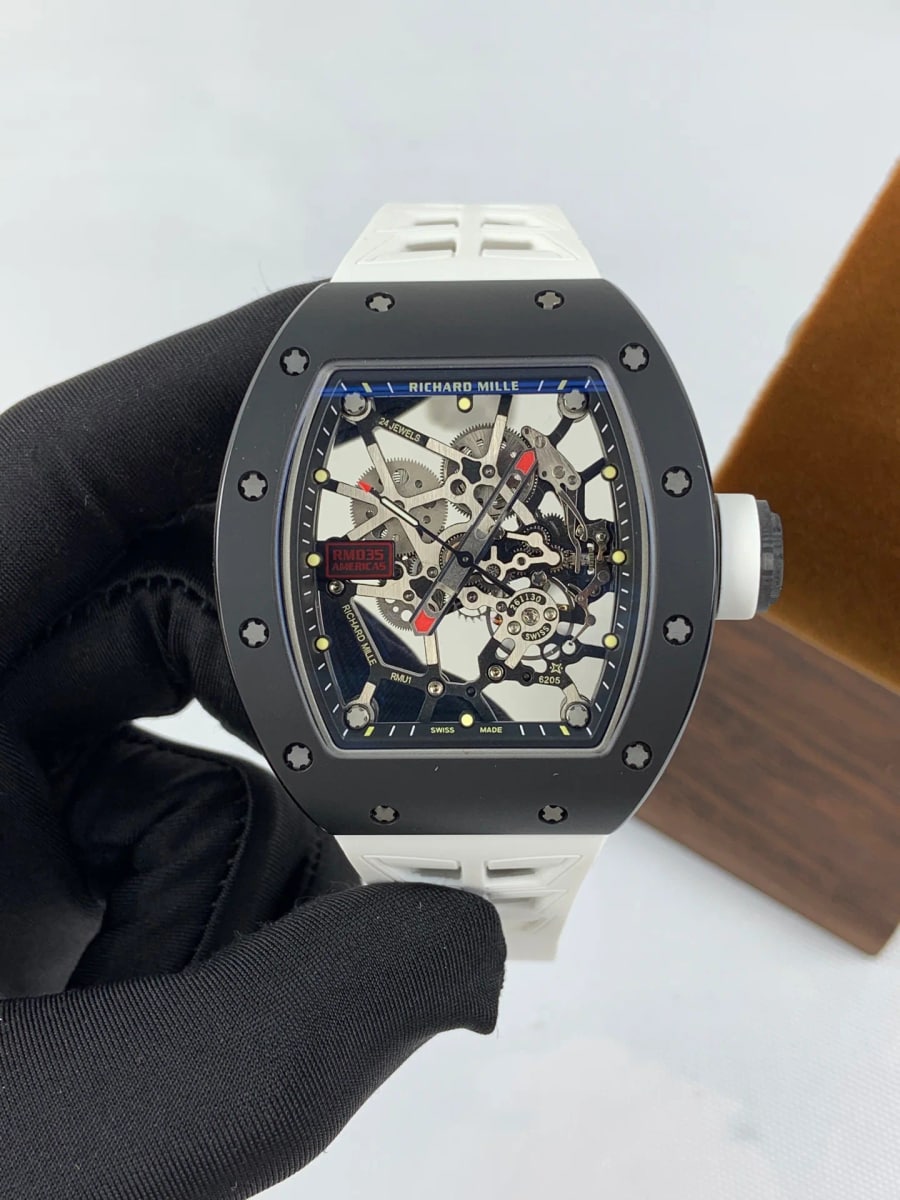 Tonneau case held upright in a black glove with a matte black bezel held by splined screws, the skeletonised movement visible under the crystal and a white strap below the case