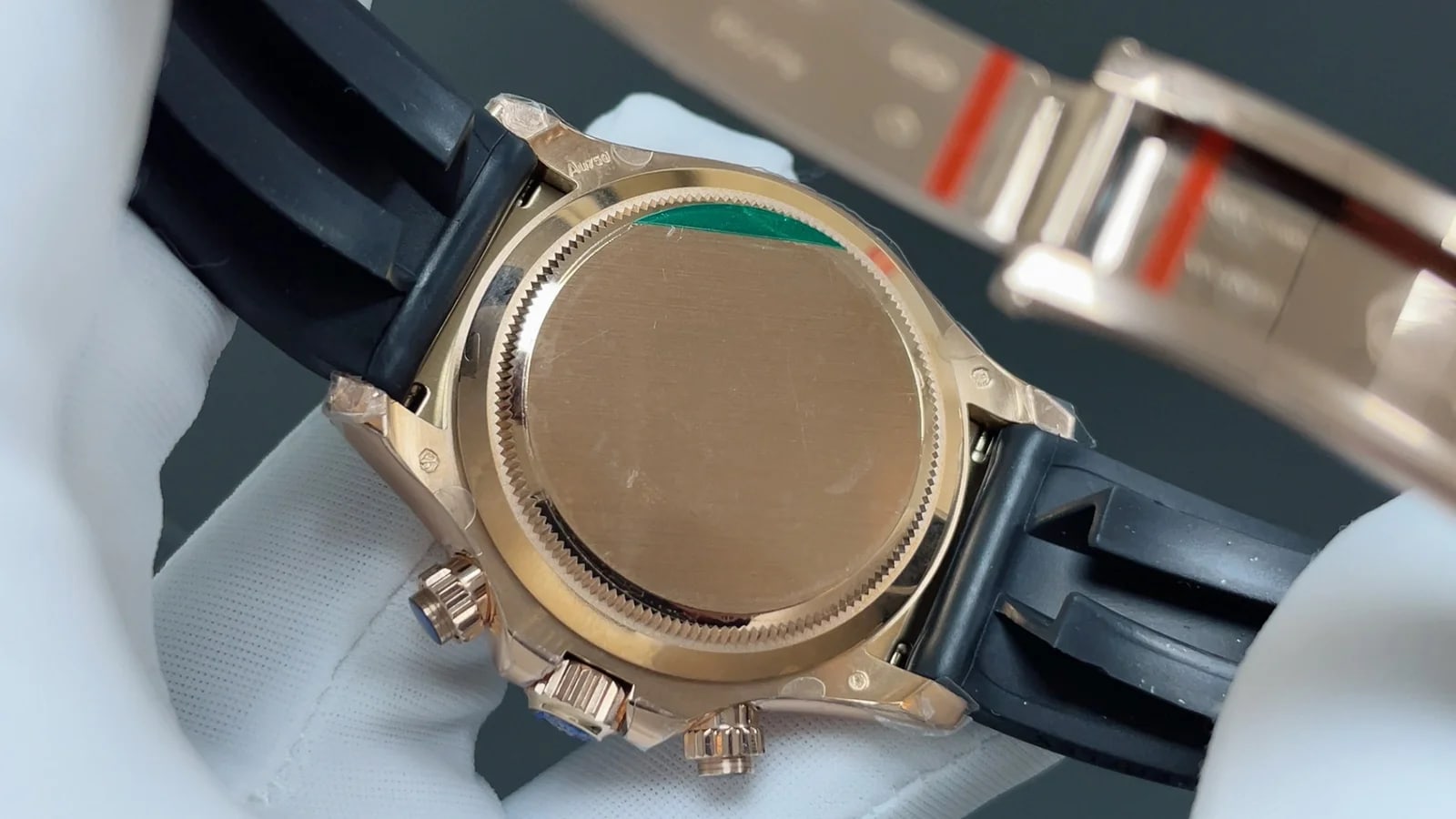 Case back detail showing the solid warm-gold back with its sticker, the pushers either side and the folding clasp of the strap