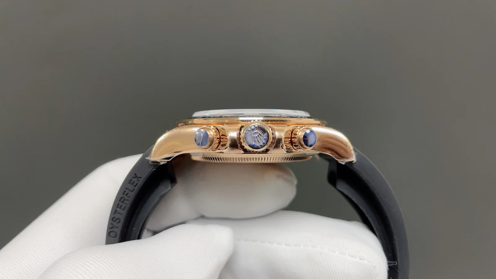 Case side profile with the crown between the two pushers, the black bezel edge above them and the rubber strap curving away from the lugs