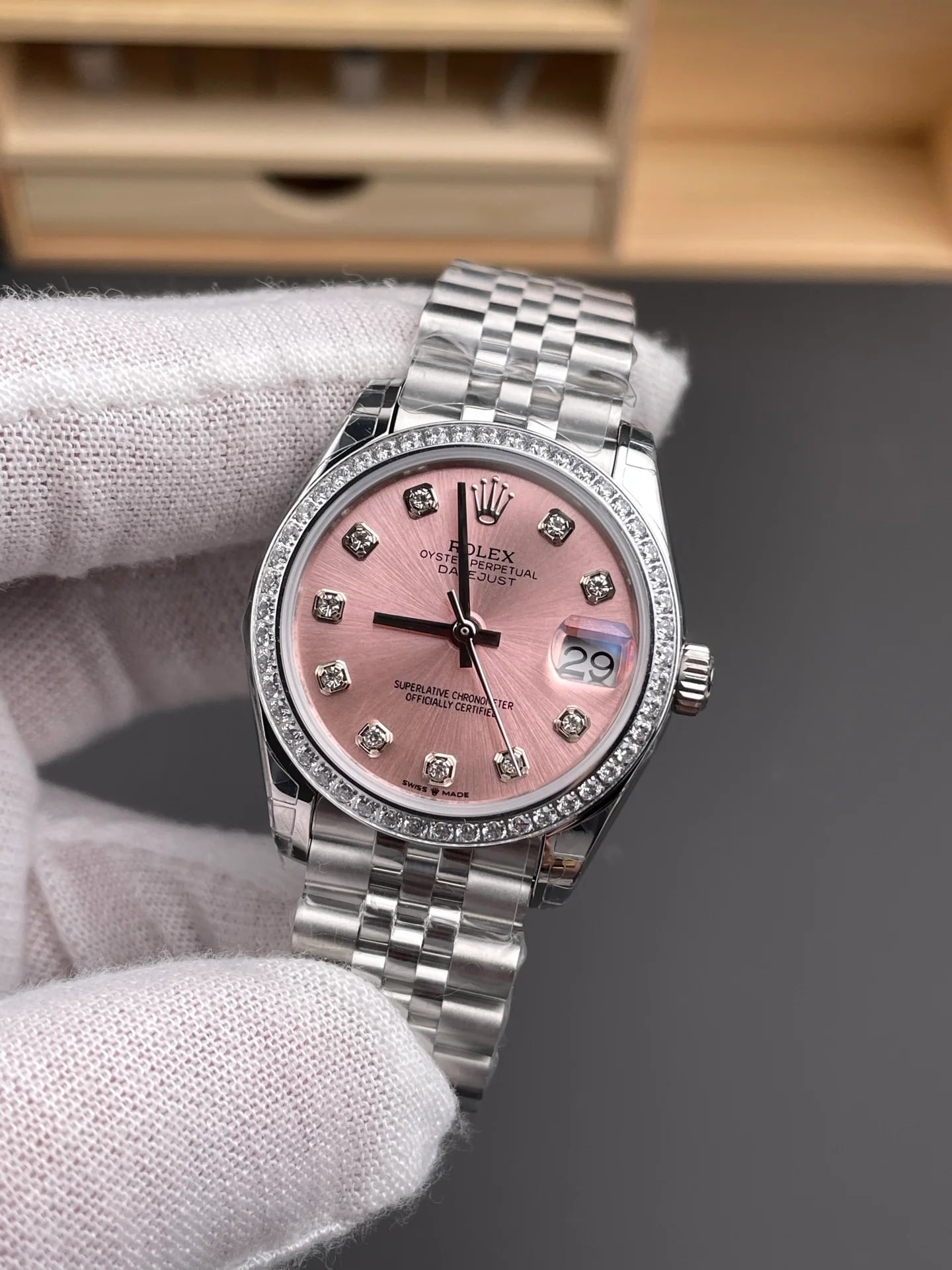 Pink dial with stone markers straight on inside the stone-set bezel, with the date under its magnifier and the five-link bracelet below