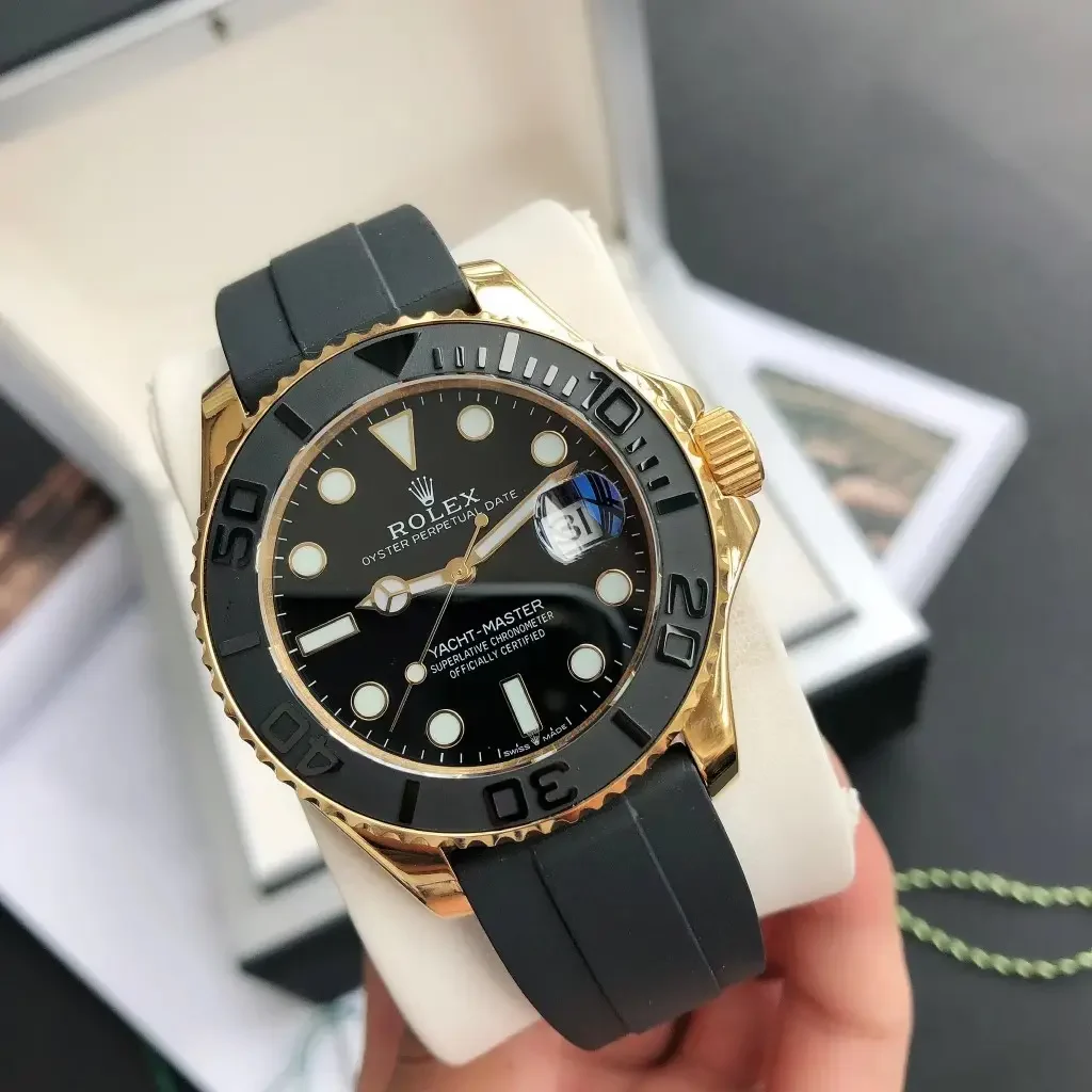 Three-quarter view with the raised bezel numerals catching the light, the black dial below and the folding clasp of the black strap in the foreground