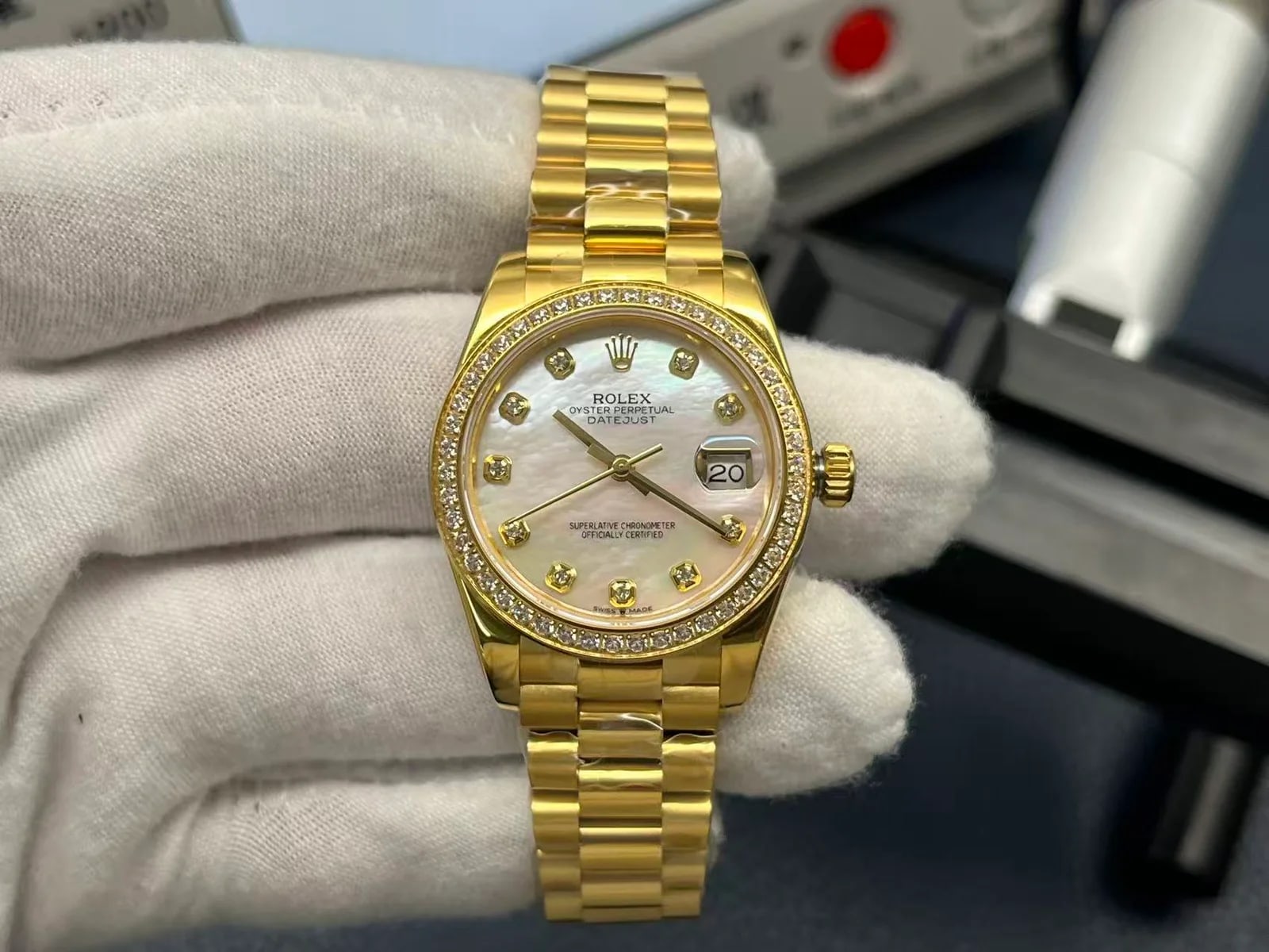 Mother-of-pearl dial with stone markers straight on inside the stone-set gold bezel, with the date under its magnifier and the three-piece bracelet below