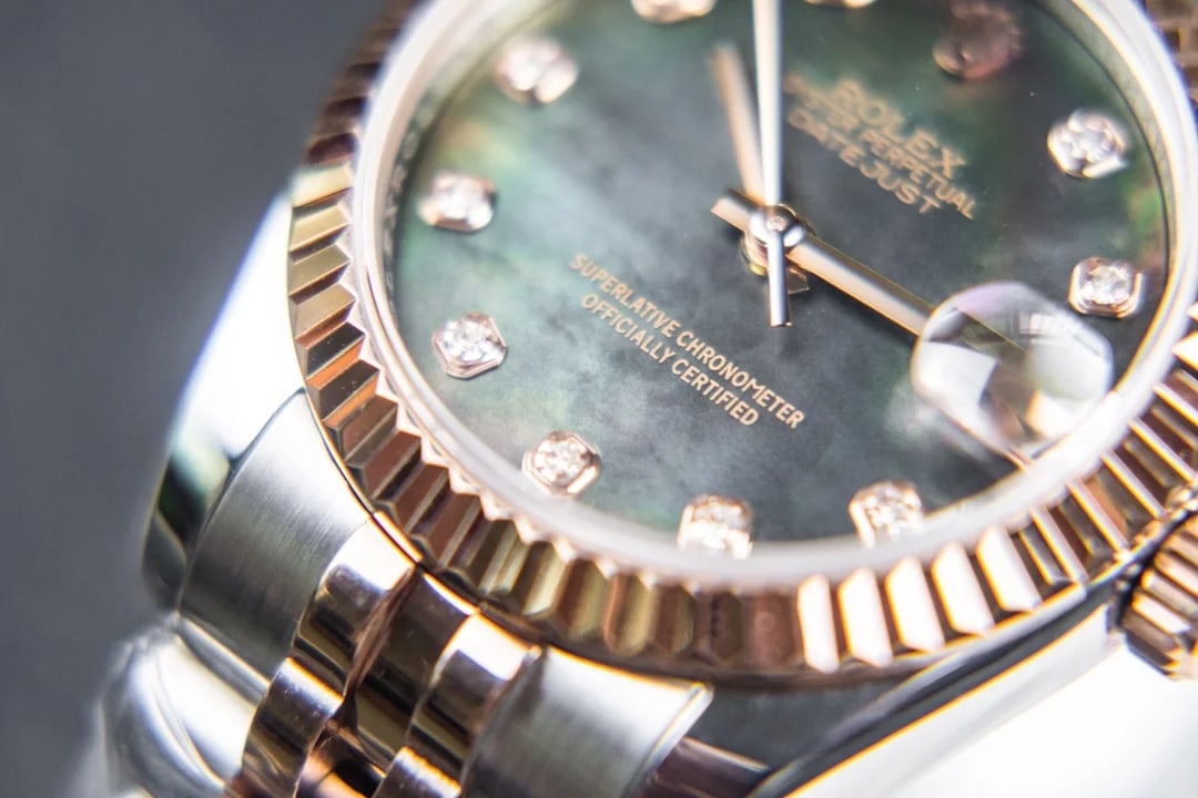 Dial close-up of the mother-of-pearl surface with its stone markers and the fluted bezel beside them, showing the colour shift across the material
