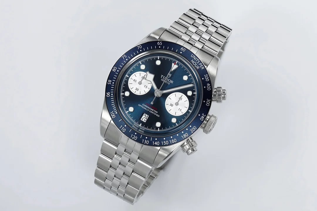Angled three-quarter view: the dial turned so both silver counters shorten into ellipses, the blue bezel insert and its silver markings, the crown and both pushers off the right flank, bracelet folding under the case