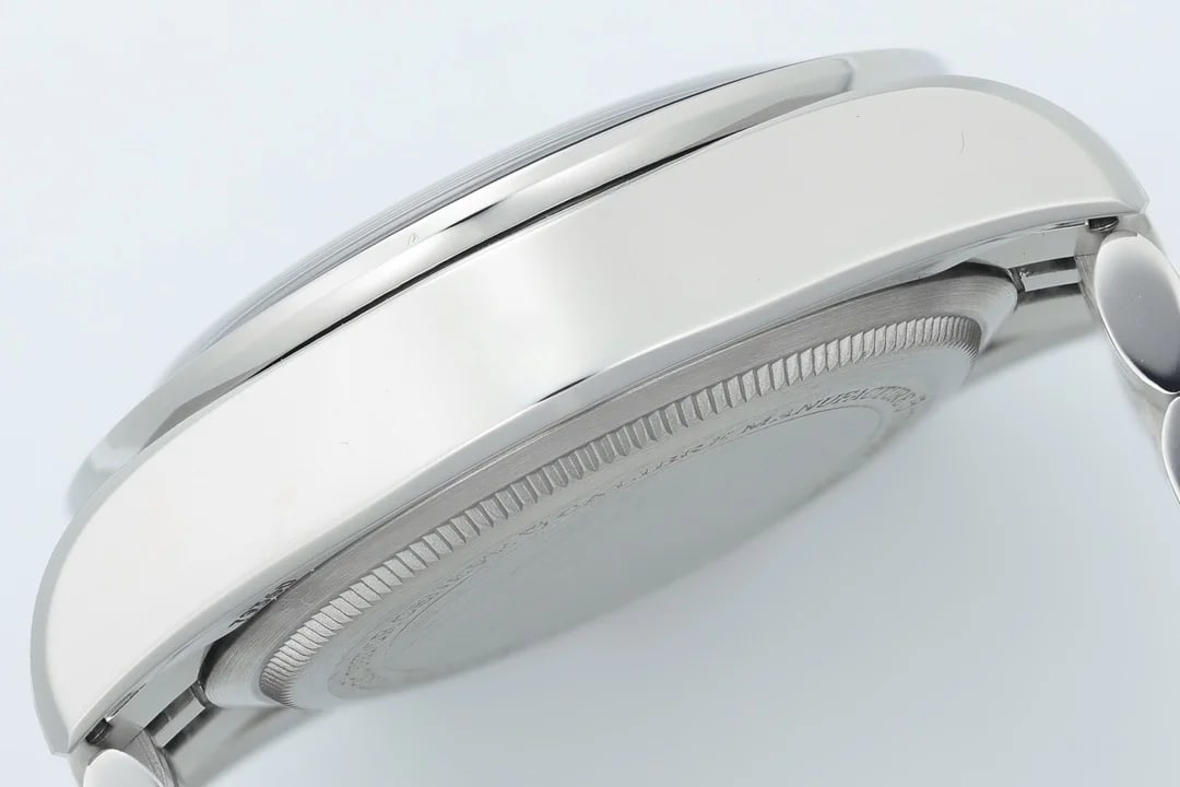 Detail of the case from the side: a smoothly polished flank running into a finely fluted back rim, bracelet end links turned away at one edge, no lettering legible on the back, pale grey background
